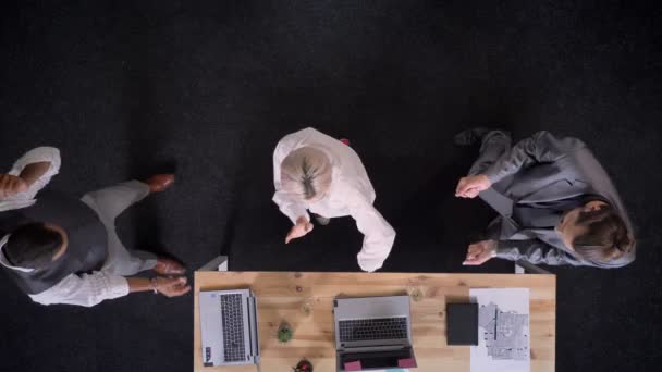 Tres trabajadores multiétnicos están bailando cerca de la mesa con computadoras portátiles y copas con champán en la oficina, concepto de fiesta de la empresa, tiro superior — Vídeos de Stock