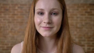 Genç taze zencefil kız kameraya, tuğla arka plan izliyor