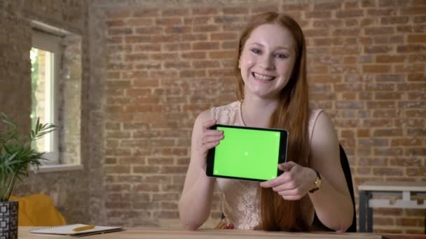 Joven chica pelirroja fresca está mostrando la pantalla verde en su tableta, mirando a la cámara, concepto de comunicación, fondo de ladrillo — Vídeos de Stock