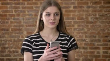 Genç tatlı blonda tipik smartphone, düşünme kavramı, iletişim kavramı, tuğla arka plan üzerinde haber