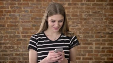 Genç tatlı blonda rüya kavramı, iletişim kavramı, tuğla arka plan smartphone üzerinde ileti yazmakta olduğunu