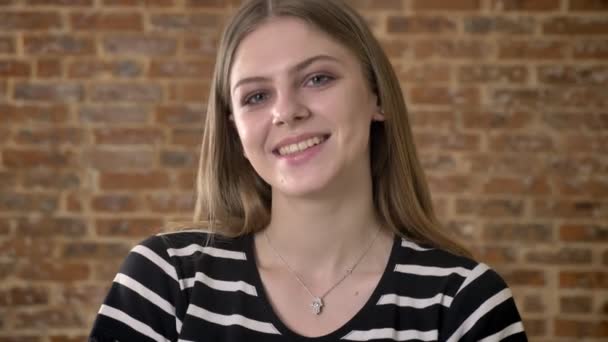 Jeune charmante blonda regarde à la caméra, souriant, fond de brique — Video