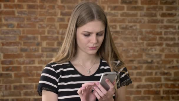 Jeune blonda douce tape message sur smartphone, dégoûtant, concept de communication, fond de brique — Video