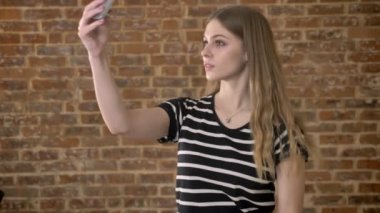 Genç mutlu blonda selfie smartphone, iletişim kavramı, tuğla arka plan yapıyor