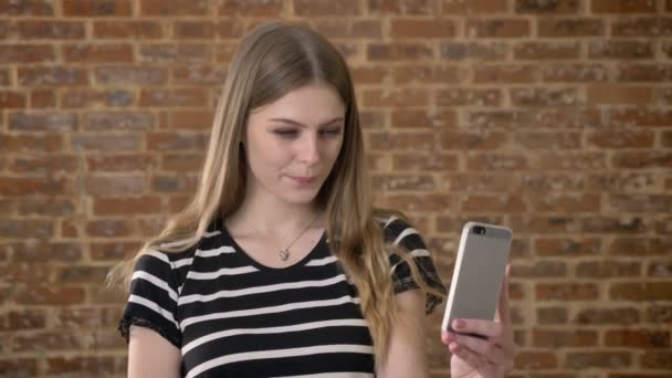 Молода щаслива блонда розмовляє у відео чаті на смартфоні, концепції спілкування, цегляному фоні — стокове відео