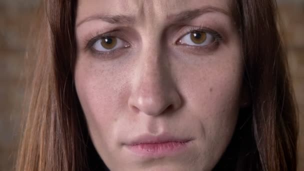 Лицо грустные каштановые волосы девушка смотрит на камеру, размытый фон — стоковое видео