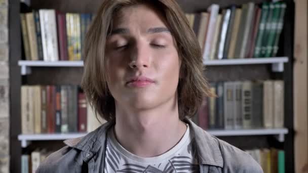 Hızma genç uzun saçlı adamla kameraya, izliyor saç tıkınma, Kütüphane arka plan bulanık — Stok video