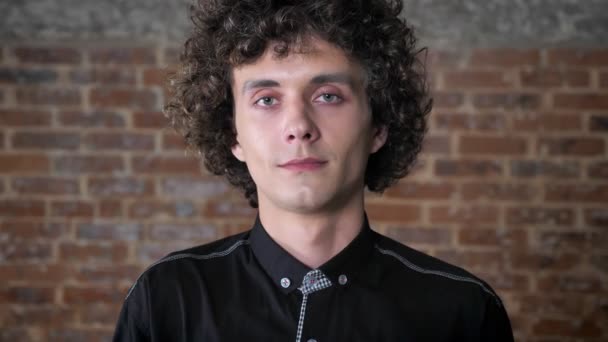 Young handsome man opening his eyes and looking at camera, smiling, brick wall background — Stock Video