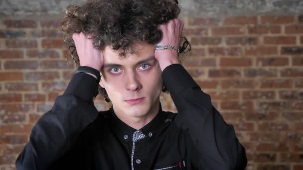 Young angry man furiously touching his hair and looking at camera with irritated expression, brick wall background — Stock Video