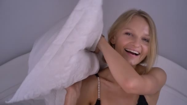 Fiatal szexi blonda nő a fehérnemű ül ágyon, párna, mosolyogva, ütő pihenni koncepció — Stock videók
