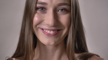 Genç neşeli kız kameraya, izlerken gülümsüyor, saç, arka plan gri