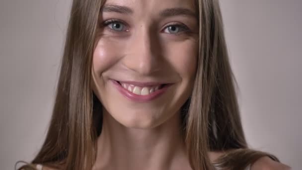 Glad flicka tittar på kameran, leende, vidröra hår, grå bakgrund — Stockvideo
