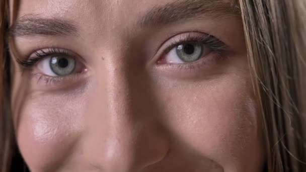 Los ojos de la joven sencere chica está mirando a la cámara, sonriendo, fondo gris — Vídeos de Stock