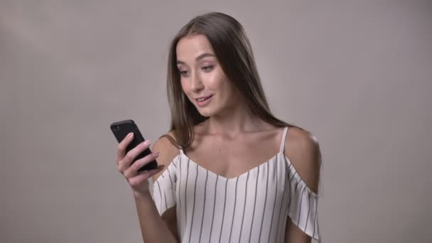 Joven chica emocionada está mostrando la pantalla verde del teléfono inteligente, mirando a la cámara, sonriendo, concepto de comunicación, fondo gris — Vídeo de stock