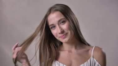 Genç seksi kız kameraya, izliyor hareketli, gülümseyen, saç dokunmadan, dudak ısırma, flört kavramı, gri arka plan