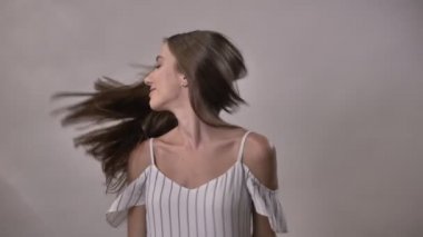 Genç güzel kız saç ile oynarken dönüyor, kameraya, gülümseyen, flört kavramı, gri arka plan izliyor