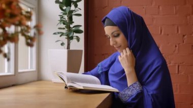 Bayan deldi burun ile büyüleyici kitap okuma ve kafede oturan mavi hijab genç güzel kadın.