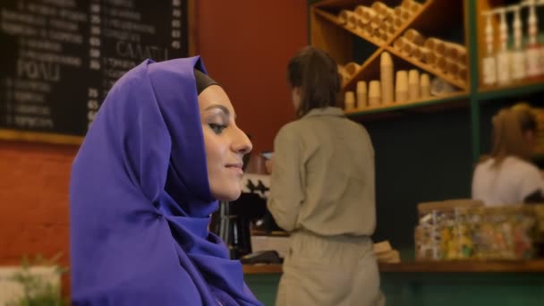 Wanita muslim muda dalam hijab duduk di restoran dan tersenyum di depan kamera — Stok Video