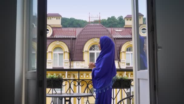 バルコニーの上に立って、リラックス ブルーのヒジャーブの若い美しいイスラム教徒の女性 — ストック動画