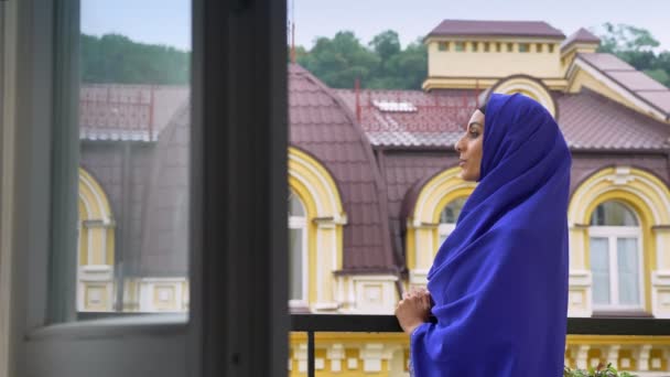 Jovem mulher muçulmana encantadora em hijab em pé na varanda e desfrutando de uma bela vista — Vídeo de Stock