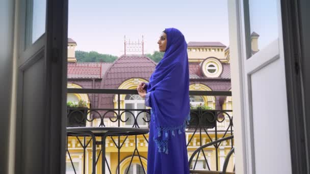 Hijab dönüm ve kameraya, güzel erkek arıyorum balkonda duran genç Müslüman kadın — Stok video