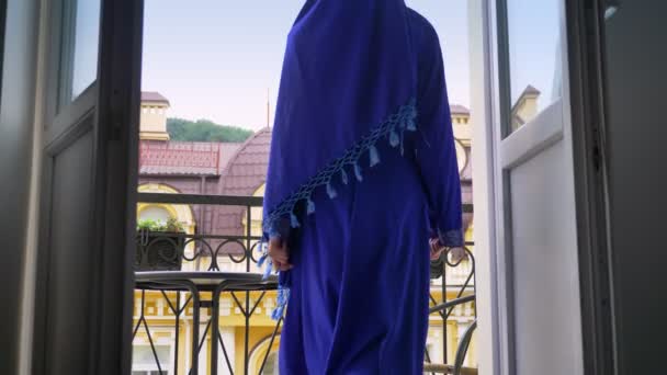 Wanita muslim muda yang cantik mengenakan jilbab pergi ke balkon dan berdiri di sana, profil wanita menawan — Stok Video