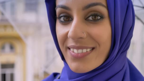 Retrato de una joven musulmana en hijab sosteniendo el paraguas y sonriendo a la cámara, hermosa hembra con la nariz perforada — Vídeo de stock