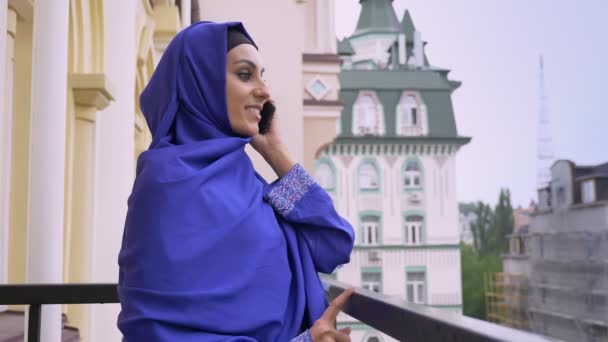 Jovem mulher muçulmana bonita em hijab de pé na varanda e falando ao telefone durante a chuva — Vídeo de Stock