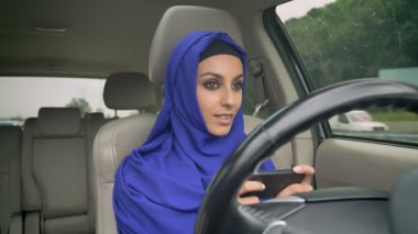Kendi kendine sürüş direksiyon özerk otomatik pilot sürücüsüz otomobil oturan ve cep telefonundan yazarak hijab genç Müslüman kadın