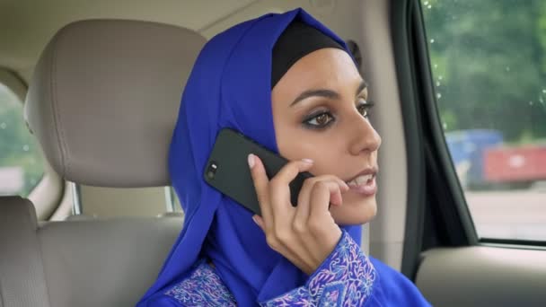 Fiatal muzulmán nő ül a hátsó ülés utasok autó és beszél a mobiltelefonján, hidzsáb mosolyogva — Stock videók