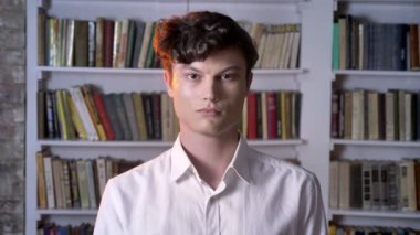 Ciddi esmer adam kamera, arka plan üzerinde Kütüphane izliyor