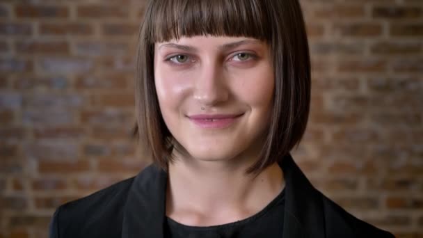 Jovem mulher feliz com corte de cabelo curto olhando para a câmera e sorrindo, isolado no fundo de tijolo — Vídeo de Stock