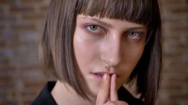 Junge nachdenkliche Frau mit grünen Augen, die ihre Lippen berühren und seitlich in die Kamera schauen, Backsteinhintergrund — Stockvideo