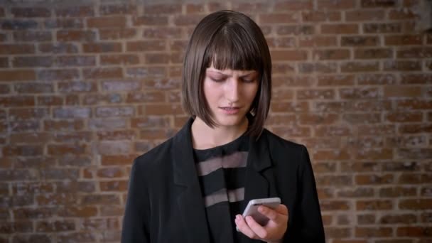 Jeune femme confus regardant téléphone avec expression déçue, isolé sur fond de brique — Video