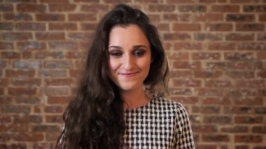 Siyah kıvırcık saçlı güzel kadın gülüyor, kameraya, tuğla arka plan izlerken