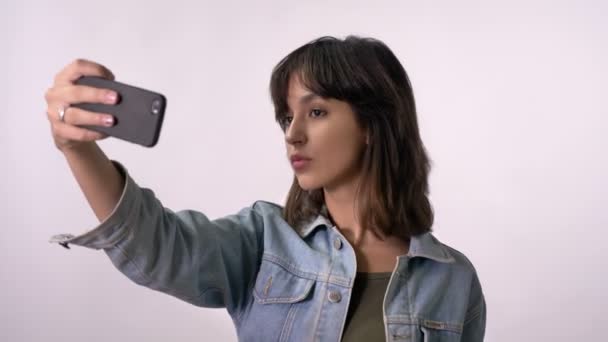 Junges brünettes Mädchen macht Selfie auf Smartphone, Entengesicht, weißer Hintergrund — Stockvideo