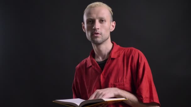 Blonde man is lezen boek, kijken in de camera, glimlachen, zwarte achtergrond — Stockvideo