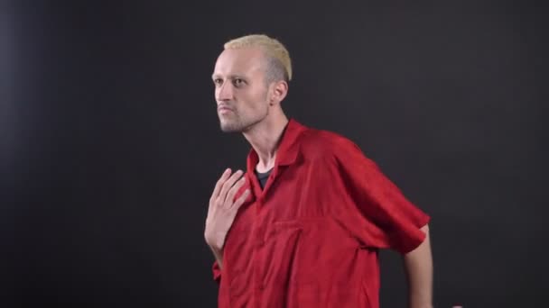 Homme blond hipsterin chemise rouge danse, concept de mouvement, fond noir — Video