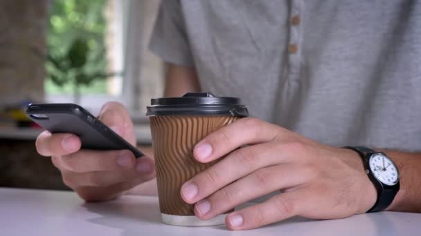 Nauwe schot van mans handen houden van koffie en typen op de telefoon in kantoor — Stockvideo
