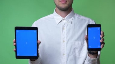 Tablet ve telefon ile chroma anahtar kamera, chroma anahtar arka plan işaret eden beyaz gömlekli sakallı genç adam