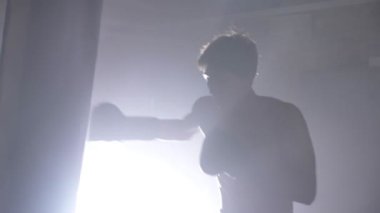 Gömleksiz kick boks siluet Boks kum torbası olarak egzersiz, karanlık odada duman ile eğitim