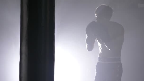 Bar överkropp kickboxare i handskar boxning slagsäck i mörka rummet med rök, sideview — Stockvideo