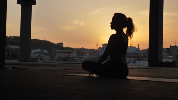 Девушка Йоги сидит в позе лотоса и меняет его в заброшенном здании летом на закате, здоровый образ жизни, концепция движения, концепция медитации — стоковое видео