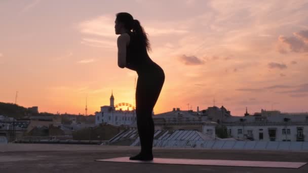 Yogi girl is standing in uttanasana on rooftop in summer on sunset, healthy lifestyle, relax concept, sport concept — Stock Video