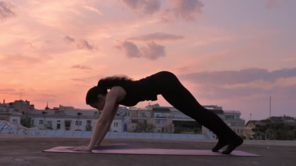 Menina Yogi está mudando poses de um peixe para um cão de pernas voltadas para baixo no telhado no verão no pôr do sol, estilo de vida saudável, conceito de relaxamento, conceito de esporte — Vídeo de Stock