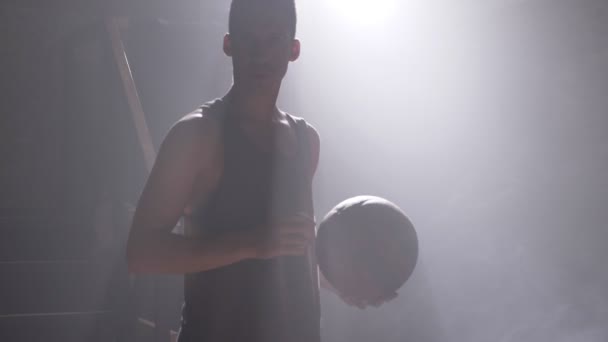 Высокий человек, играющий в баскетбол бросок в темном спортзале с дымом — стоковое видео