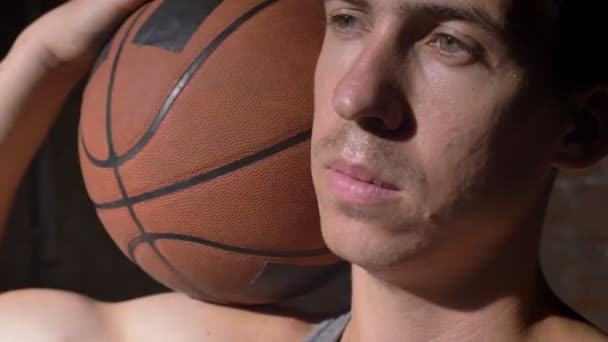 Vážné basketbalový hráč držící míč na jeho rameni a pohled z boku — Stock video