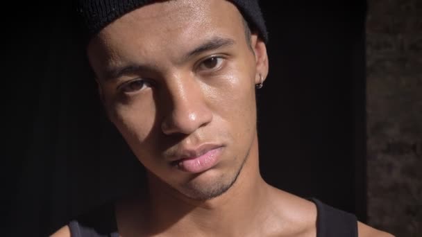 Young african-american confident man with hairband and looking at camera and standing in dark room — Stock Video