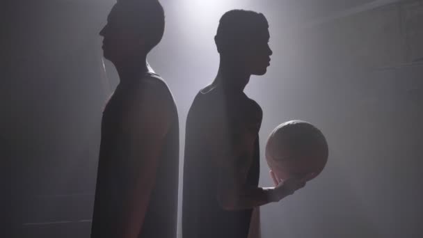 Twee basketbal spelers schaduw staan rug aan rug op mistige kamer met floodlight — Stockvideo