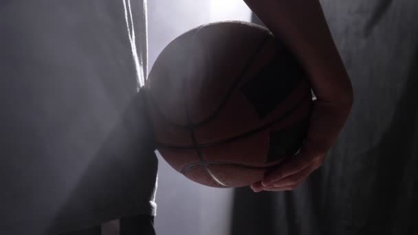 Imágenes cercanas del jugador de baloncesto sosteniendo la pelota, de pie en la habitación oscura brumosa — Vídeos de Stock